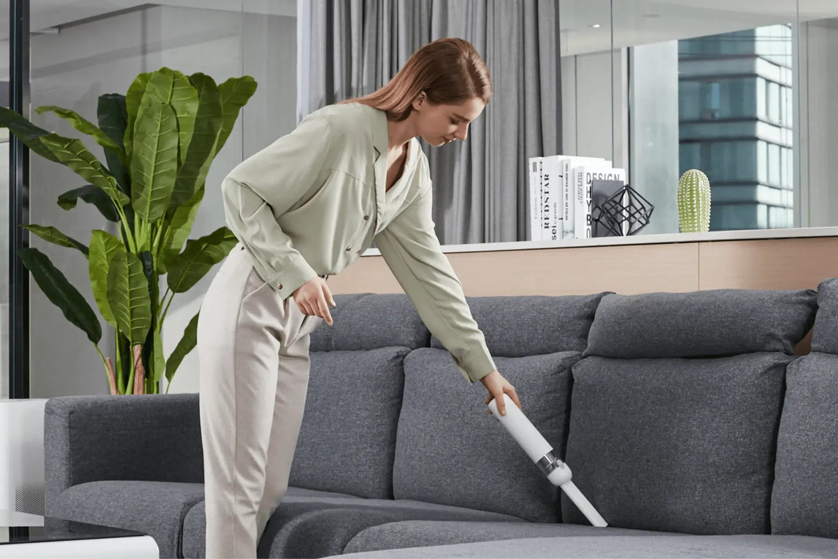 Vrouw zuigt de bank met een compacte witte Xiaomi handstofzuiger